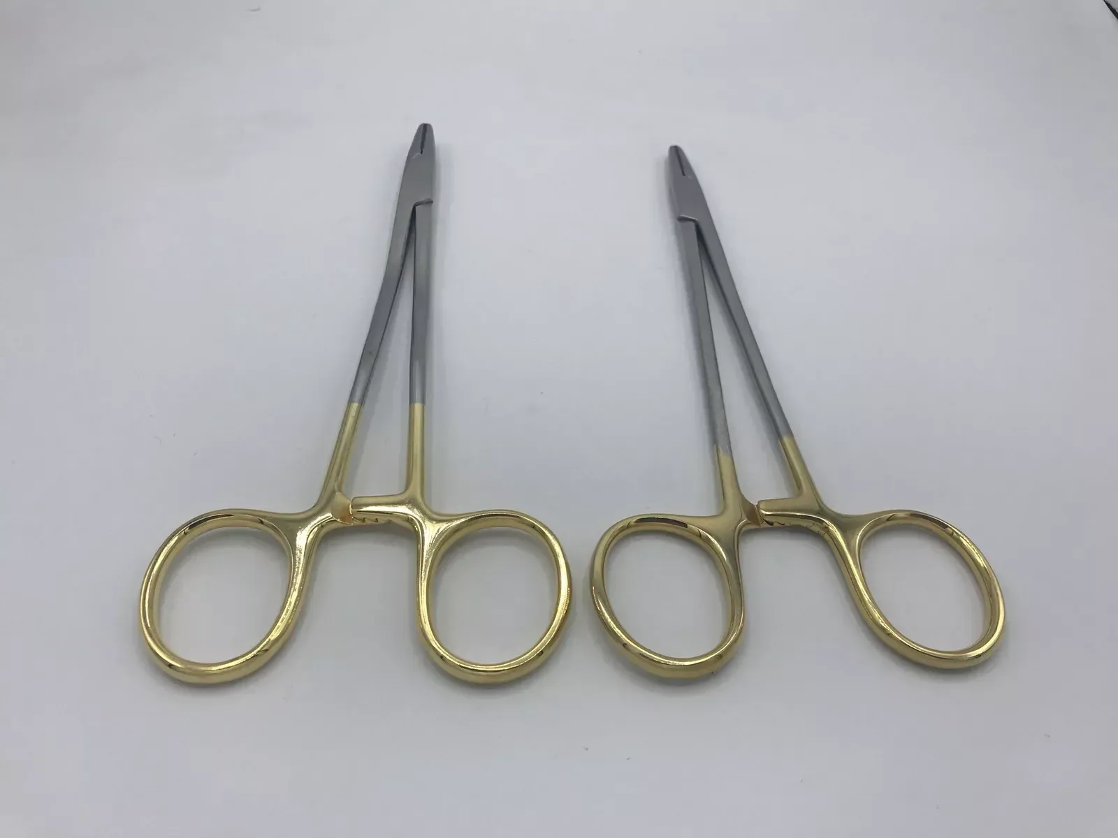 Straight and curved Mayo-Hegar needle-holder examples with gold-coloured rings — view 1